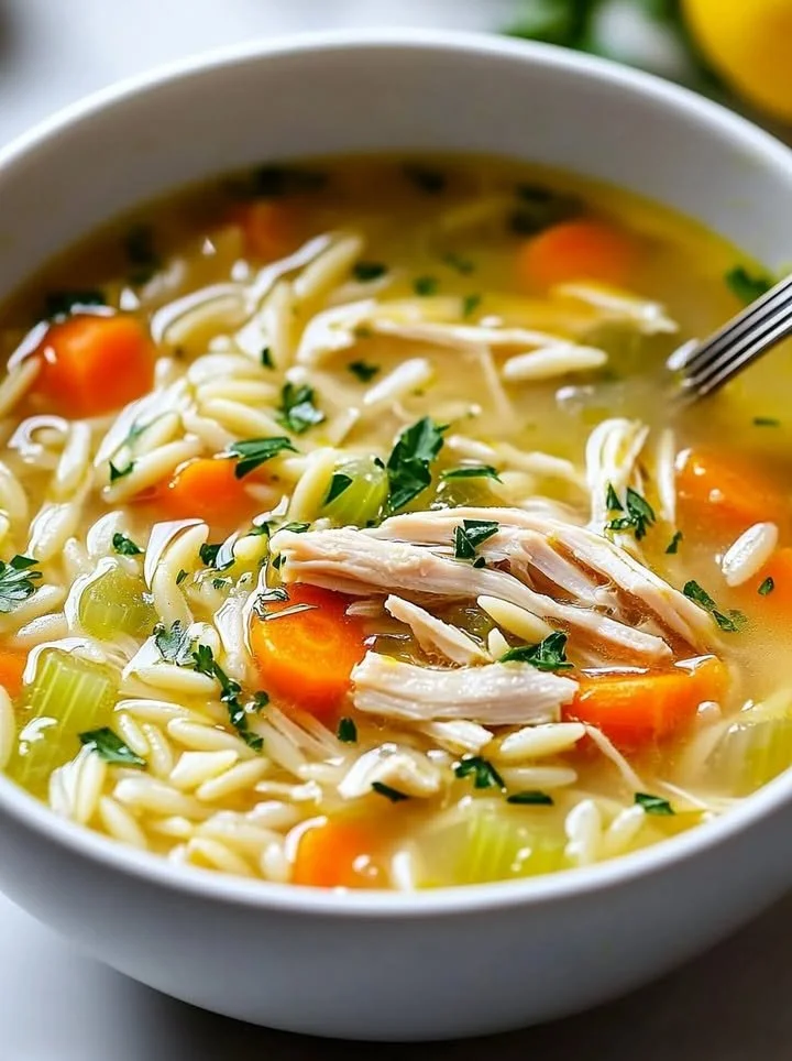 Cozy lemon chicken orzo soup with fresh herbs in a bowl