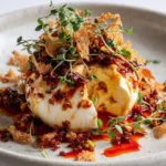 Cracked burrata with gochujang oil and pistachio brittle served on a plate